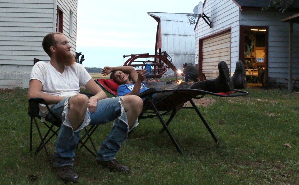 Cameron Ward, left, leagues with Kyle Staples, center, after evening chores on Sept. 30, 2015. Ryley Stringer welds farm equipment in the background and joined the conversation soon after. 